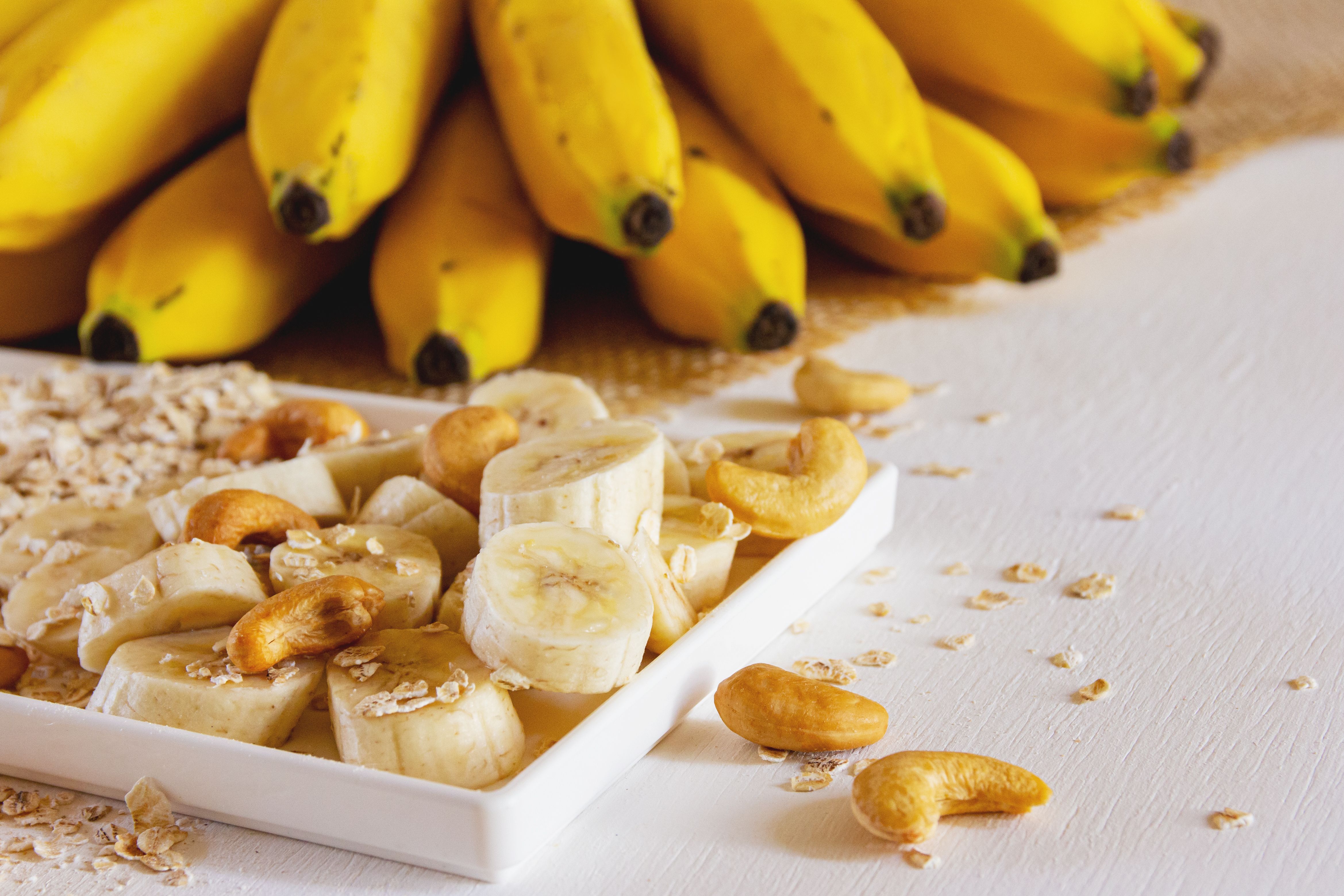 Fresh sliced bananas with cashew nuts and oats on a plate, whole bananas in the background